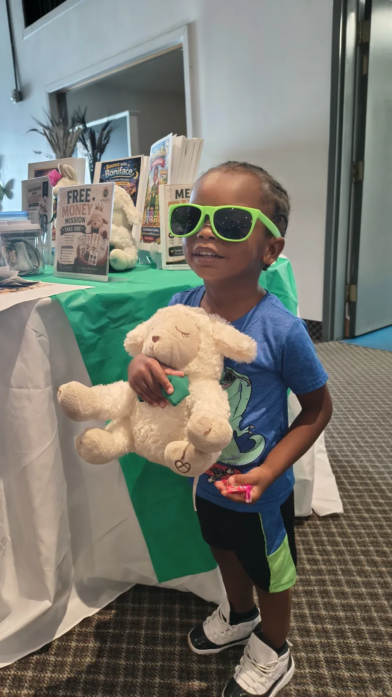 Enfant souriant avec des lunettes de soleil vertes tenant la peluche Tiro l'agneau